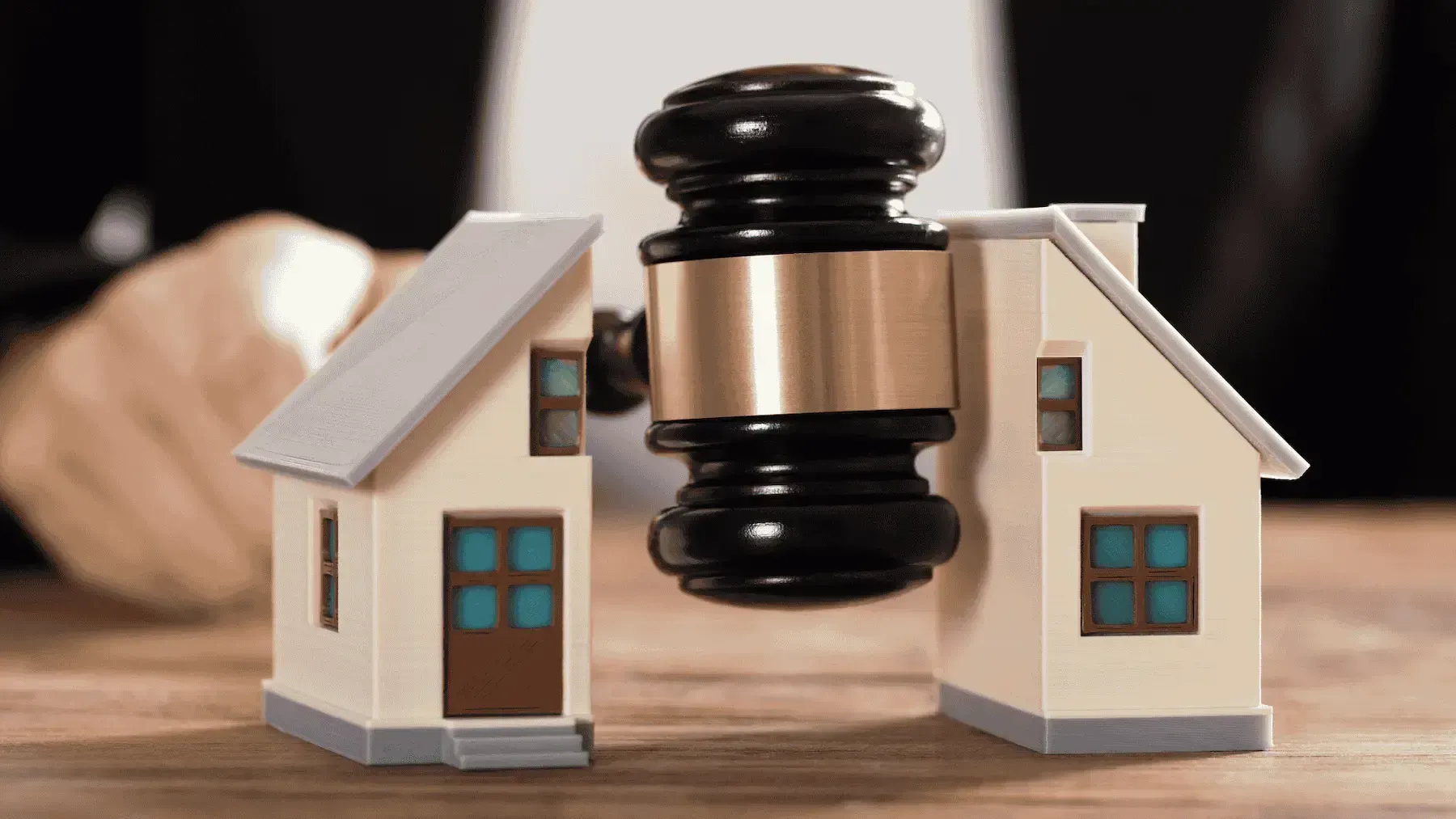 A person is holding a gavel between two small houses on a table.