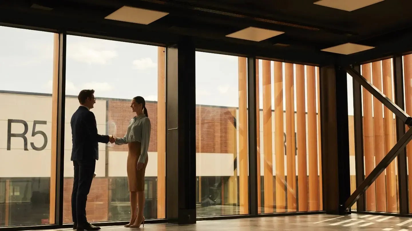 A man and a woman are shaking hands in an empty room.
