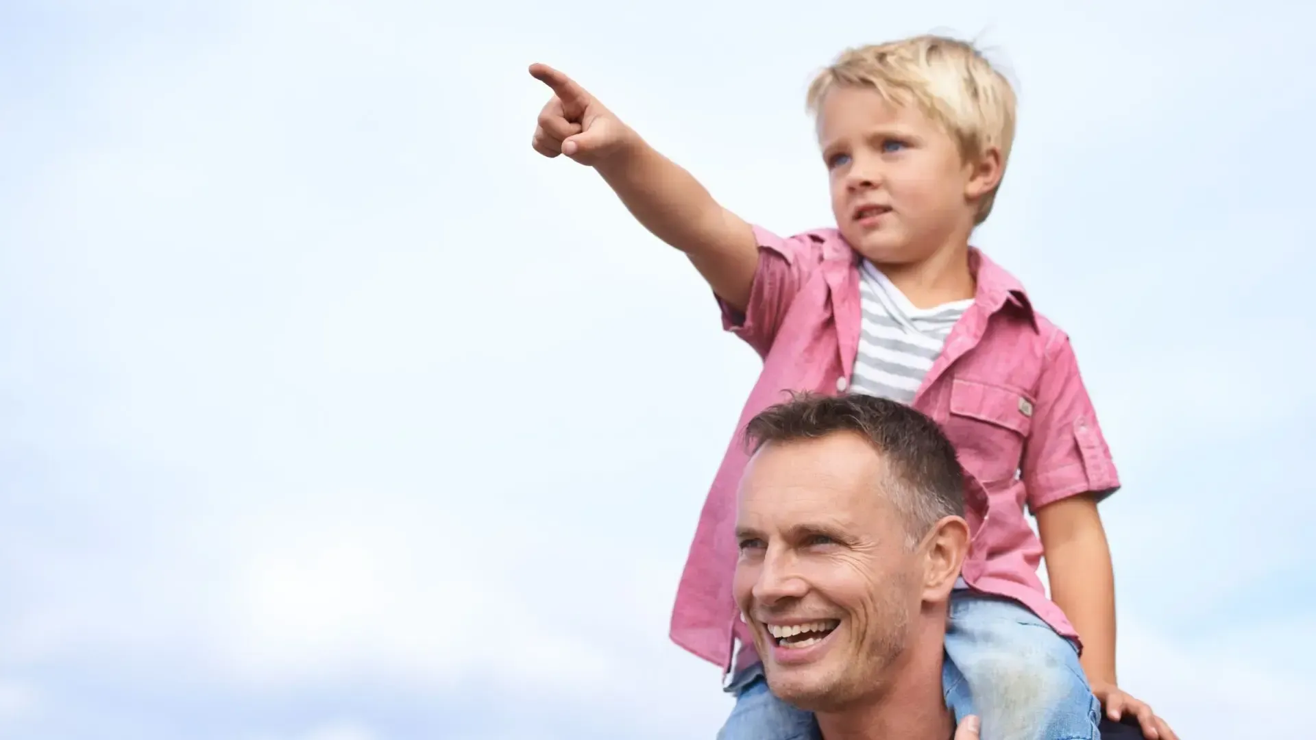 A little boy is sitting on a man 's shoulders and pointing.