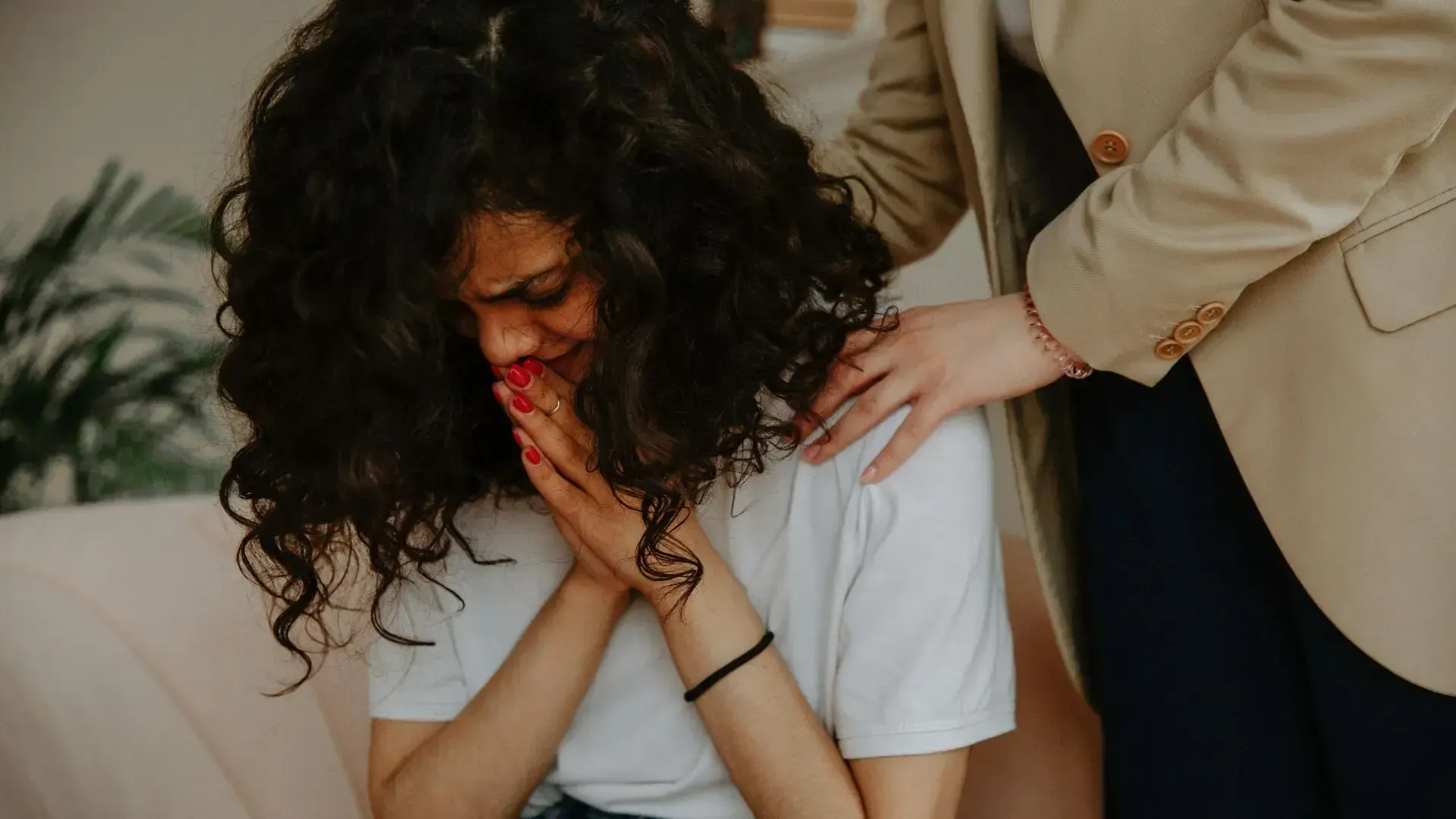 A woman is sitting on a couch with her head down and a man is comforting her.