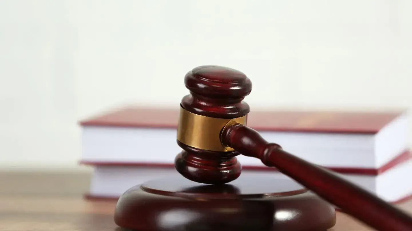 Wooden gavel on a wooden block, with two law books in the background.