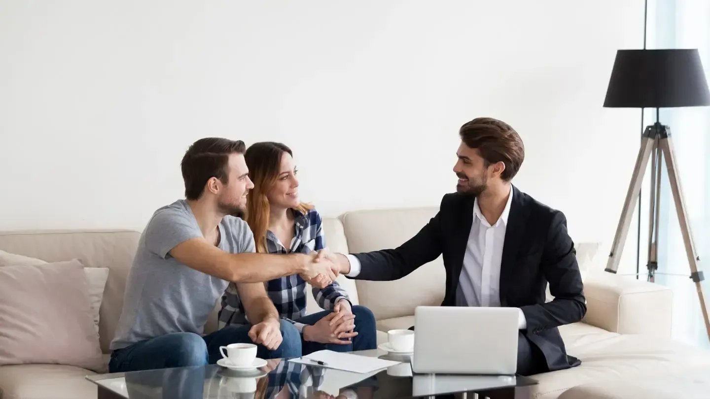 A realtor shaking hands with a couple after closing a deal on a couch.