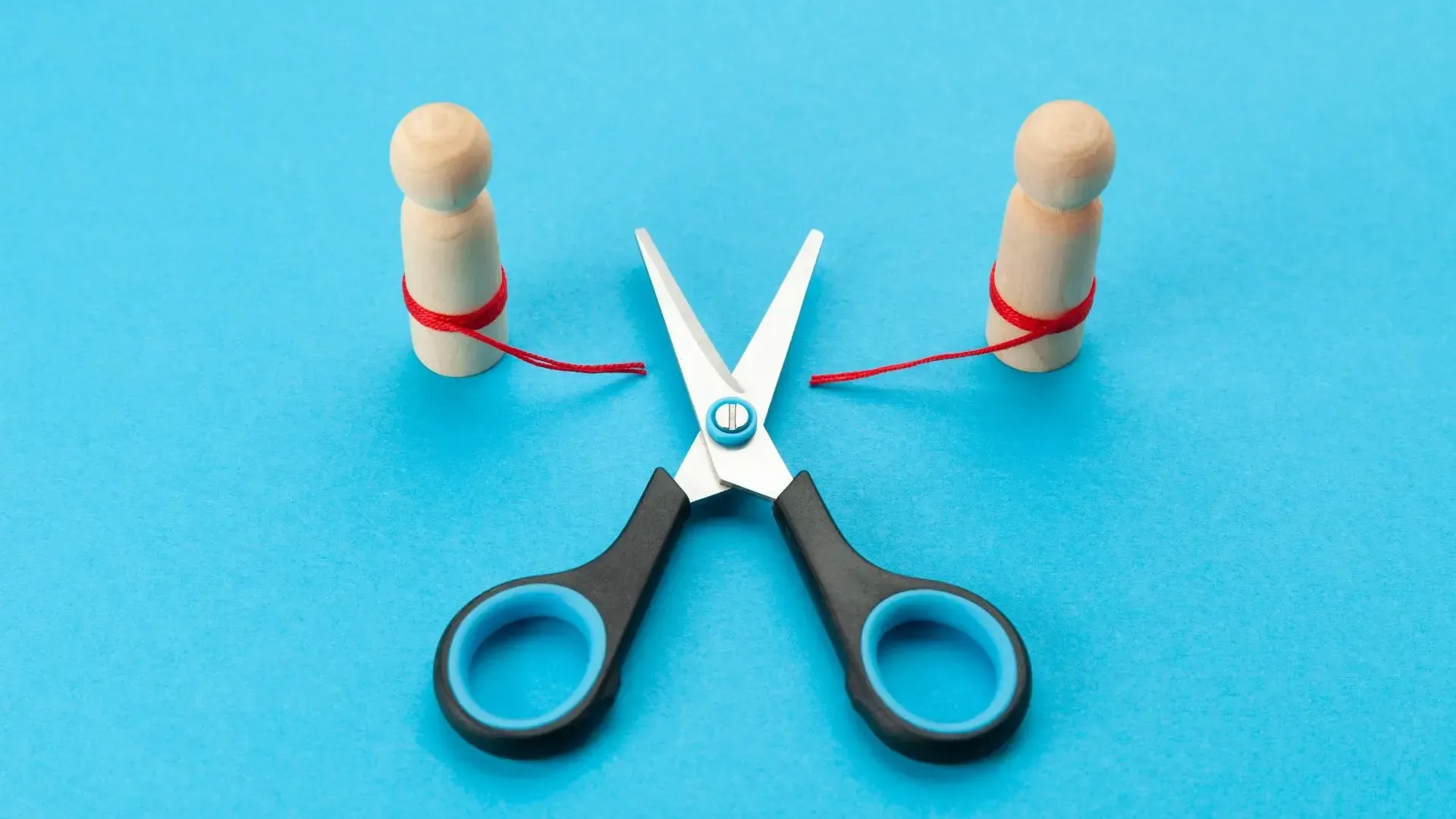 Scissors cutting red strings connecting two wooden figures on a blue background.