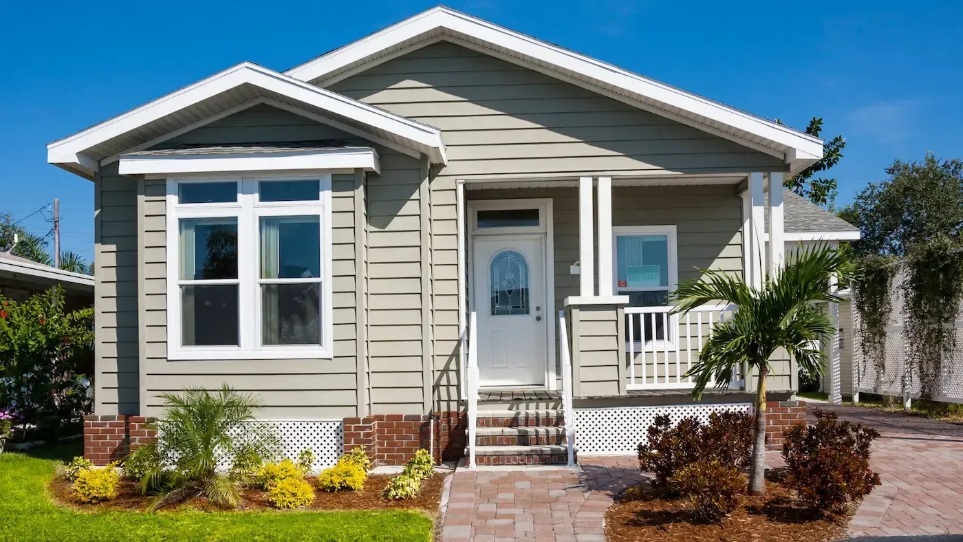 Small, light green house with white trim, a small porch, and landscaping.