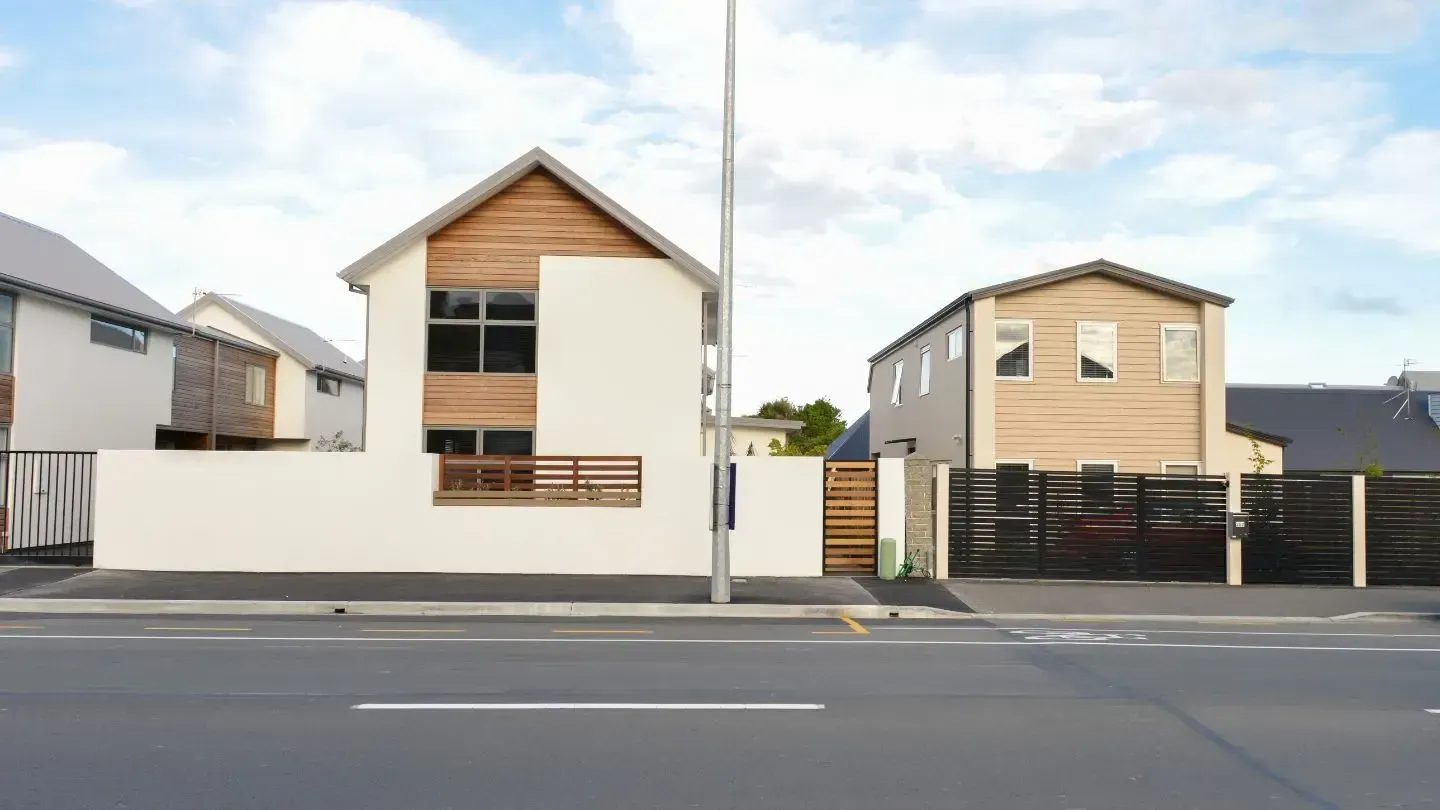 Two-story houses with wood accents and white walls near a street with a tall street light.