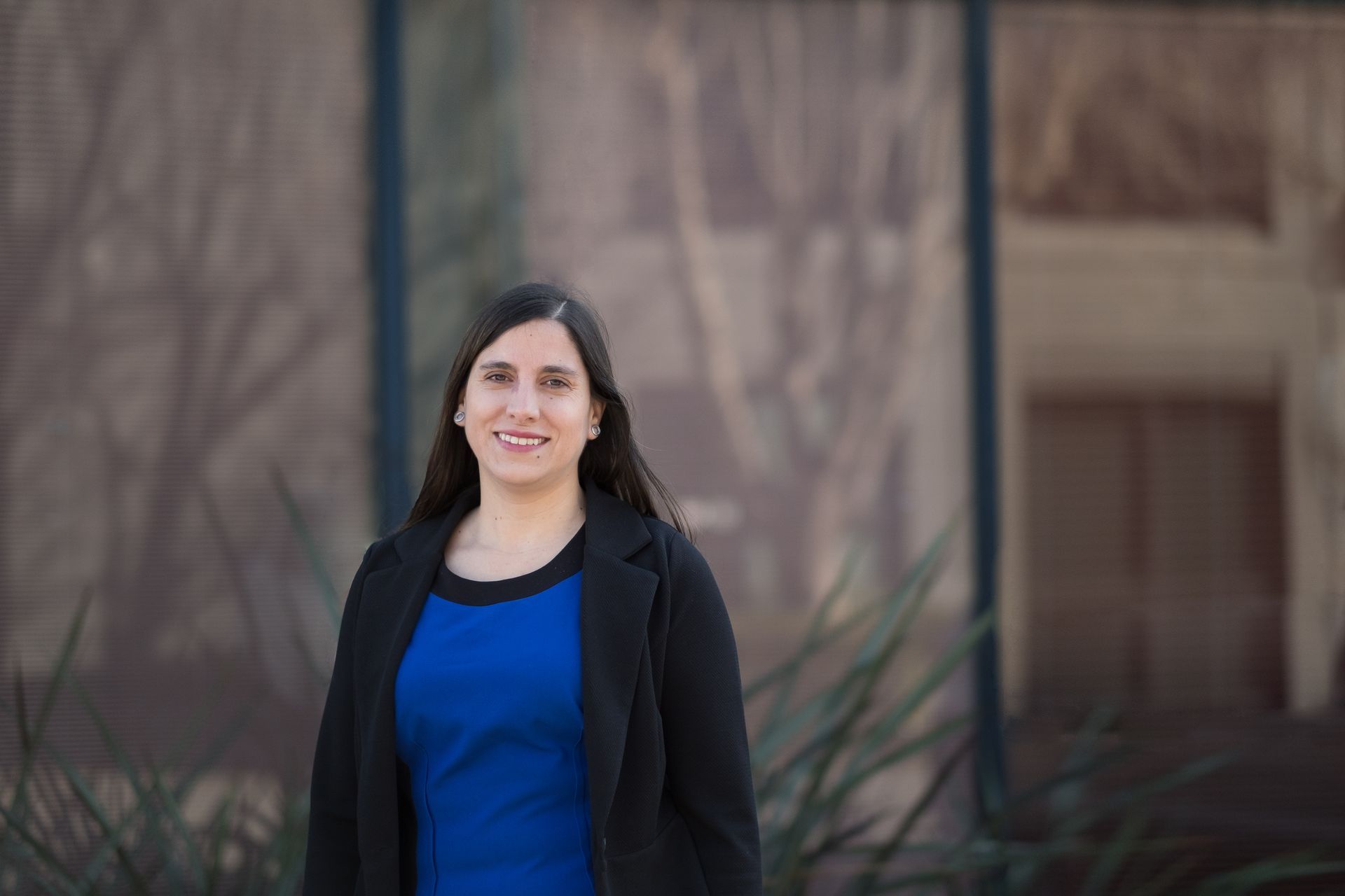 a woman in a blue dress and black jacket is standing in front of a building .