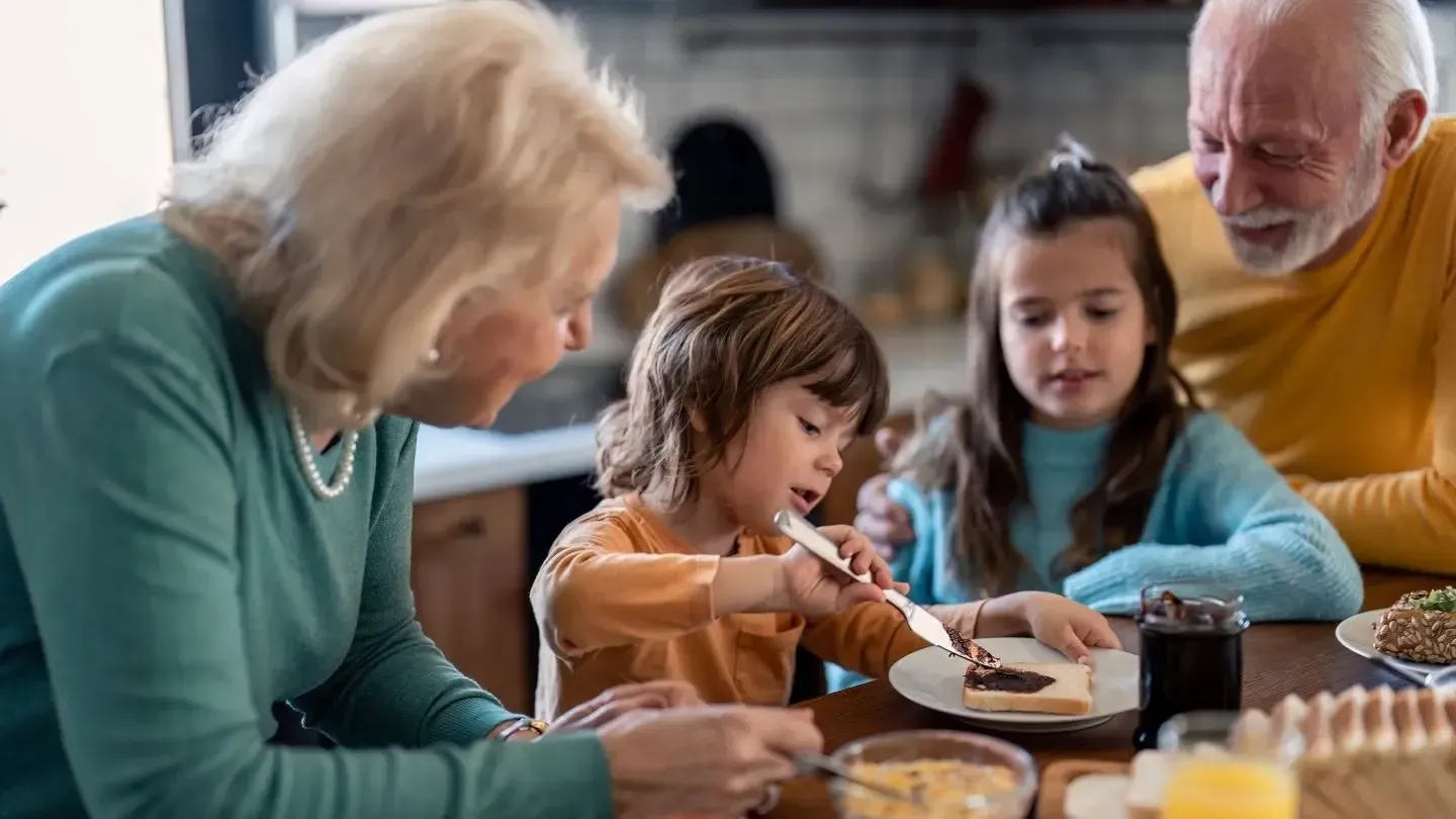 Grandparents and grandchildren at a table, spreading something on toast.