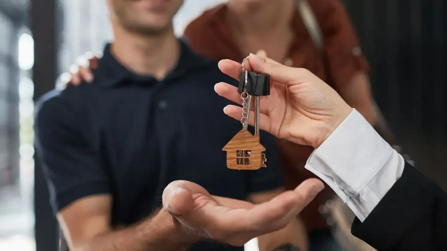 Person handing keys with house-shaped keychain to a couple.