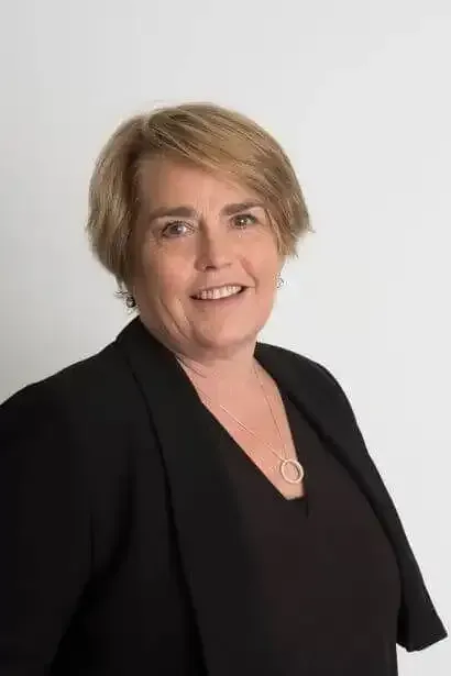 Kristy O'Connor wearing a black jacket and a necklace is smiling for the camera .