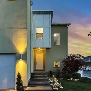 the front of a modern house with a garage and a sunset in the background .