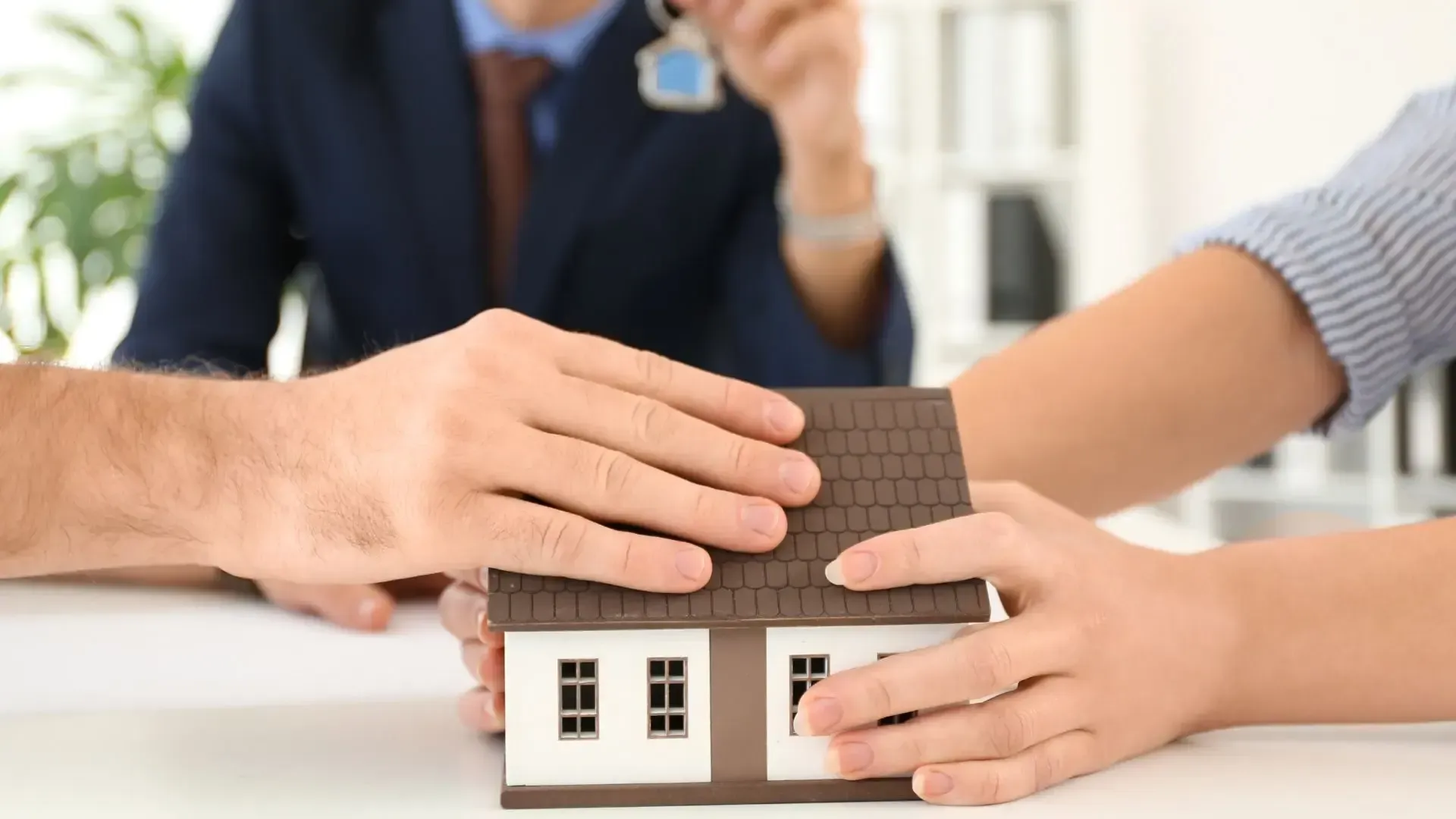 A man and a woman are holding a model house in their hands.