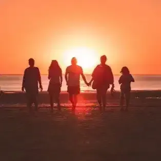 a group of people are walking on the beach at sunset holding hands .