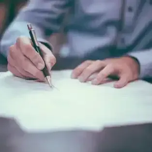 a man is writing on a piece of paper with a pen .