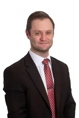 Man in a black suit with a red and white striped tie smiles at the camera.