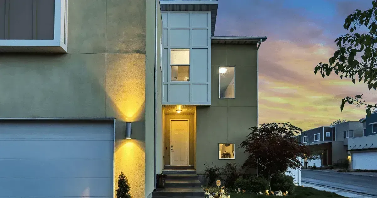 Property Lawyers Christchurch - Modern two-story house with green exterior and bright entryway, set against a colorful sunset.