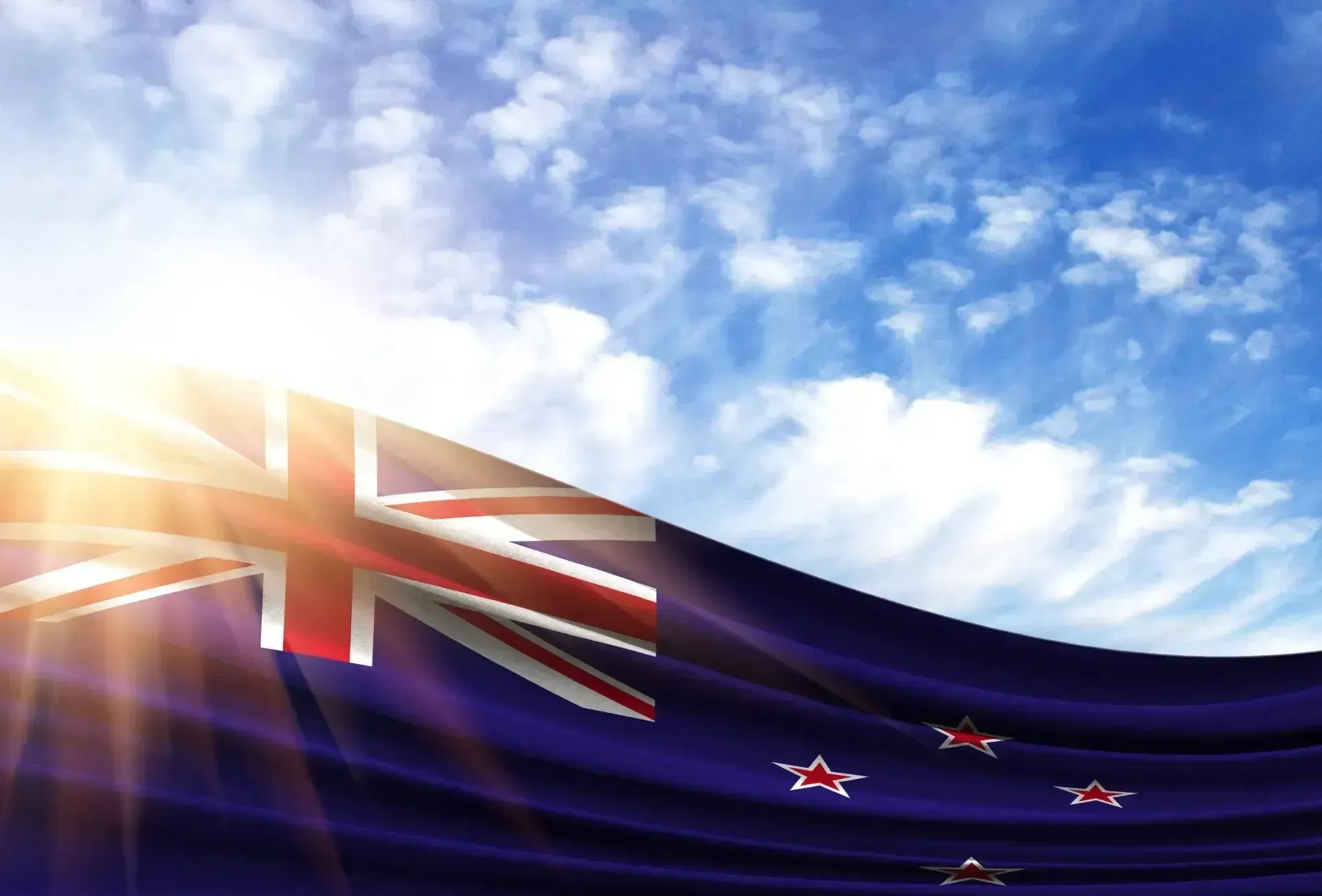 Immigration Lawyers Christchurch - New Zealand flag waving against a bright blue sky with sunbeams.