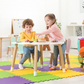Two kids playing at a white table with colorful blocks in a playroom with a floor mat.