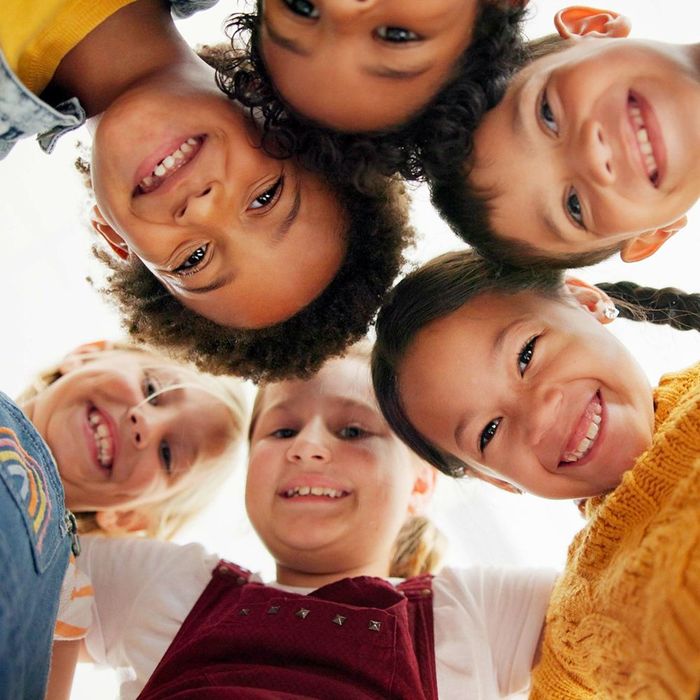 Children of diverse backgrounds smiling and looking down, forming a circle.