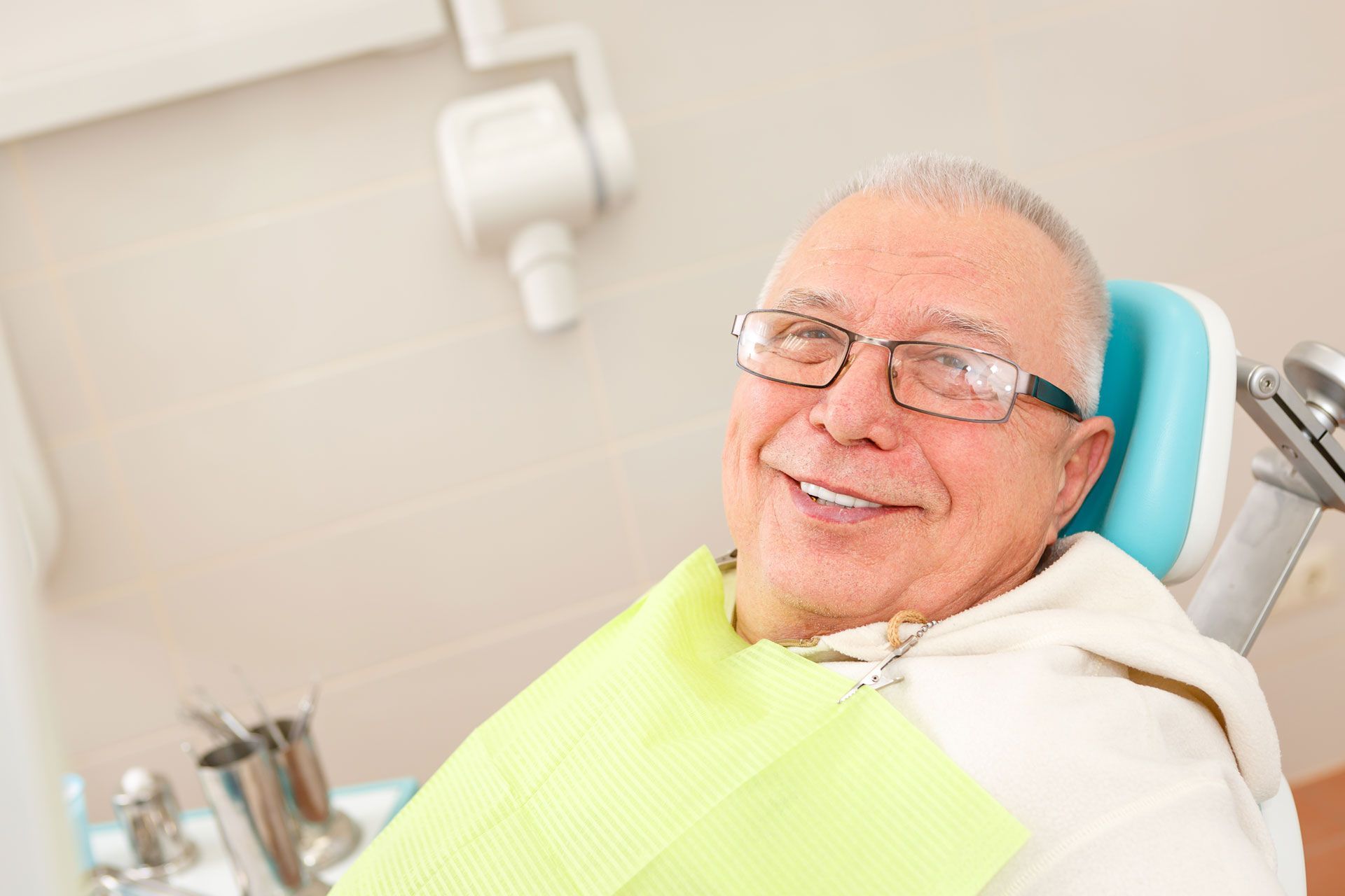 An elderly man is smiling while sitting in a dental chair.