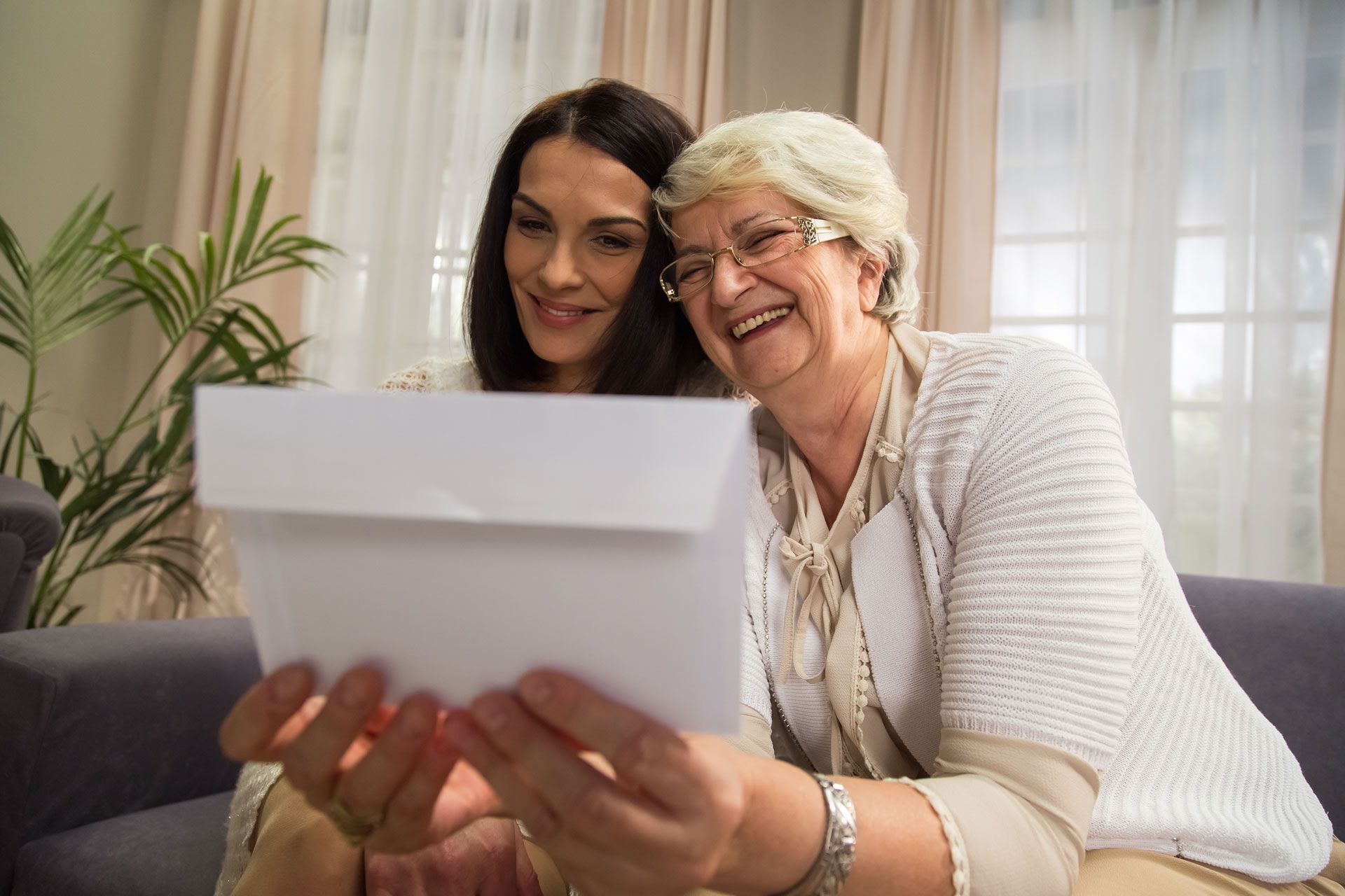 Two women are sitting on a couch looking at a piece of paper.