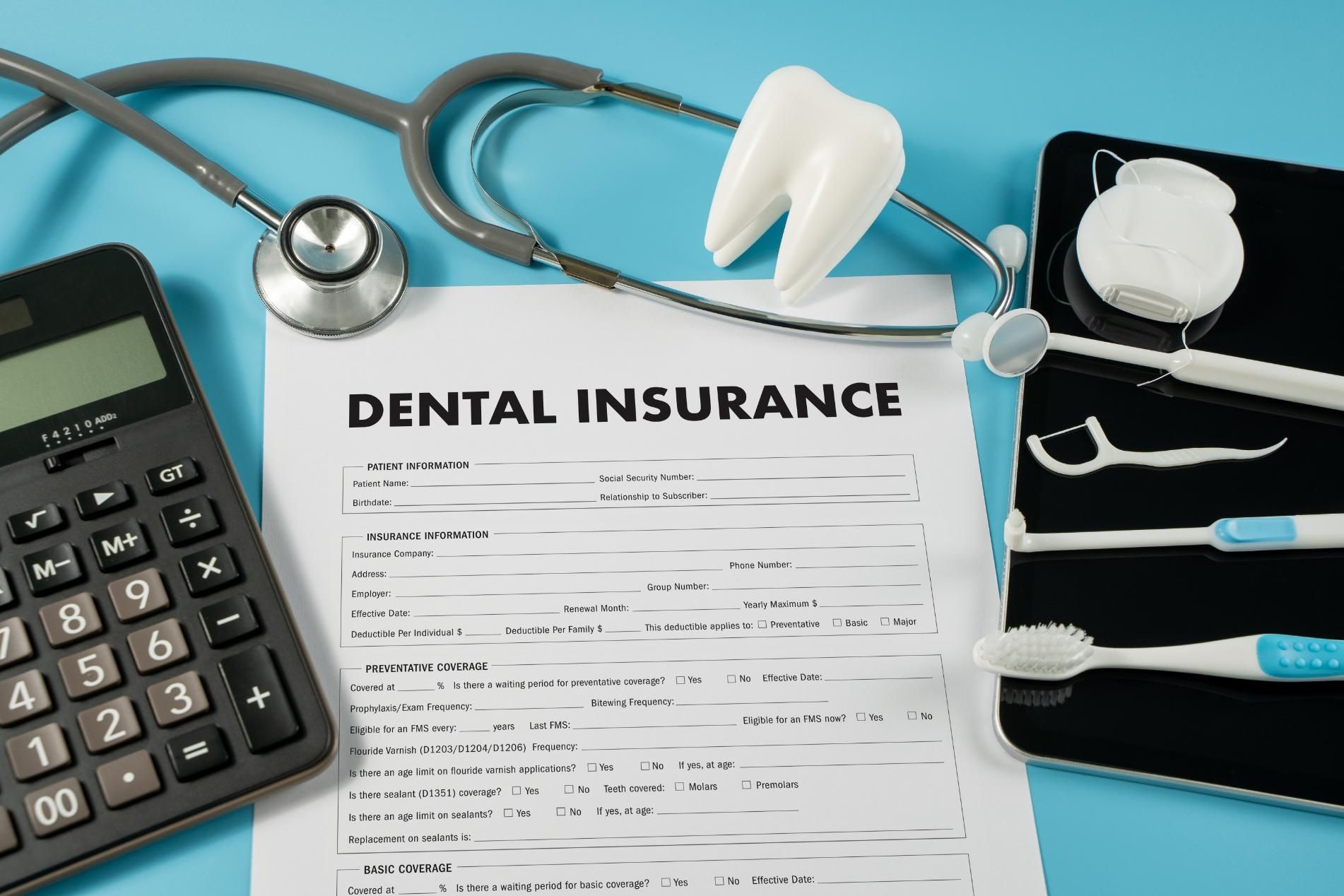 A dental insurance form with a calculator, toothbrushes, floss, and a stethoscope.