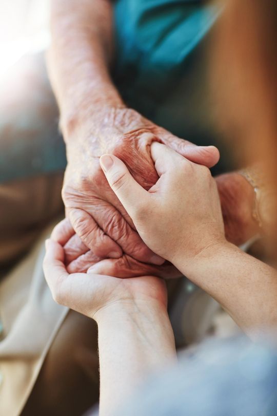 A young woman is holding the hands of an older woman.