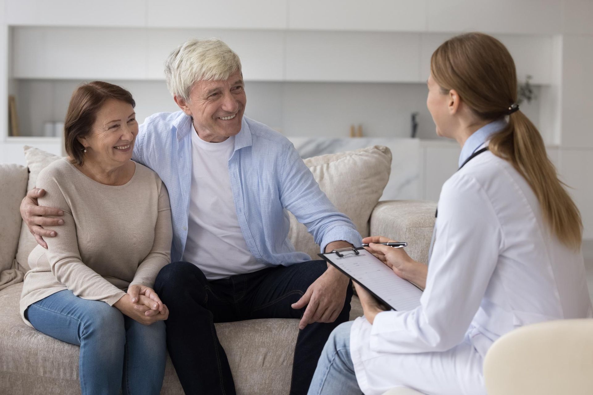An elderly couple is sitting on a couch talking to a doctor.