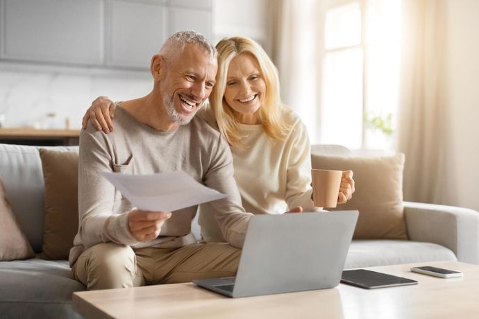 A man and a woman are sitting on a couch looking at a laptop.