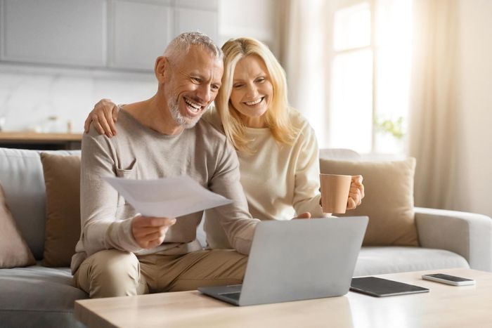 A man and a woman are sitting on a couch looking at a laptop.
