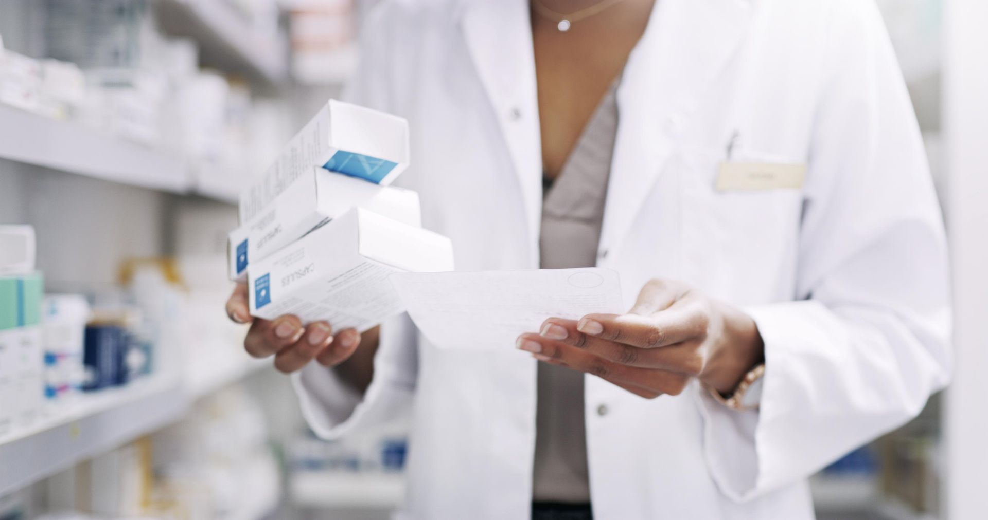 A female pharmacist is holding a stack of boxes in her hands in a pharmacy.