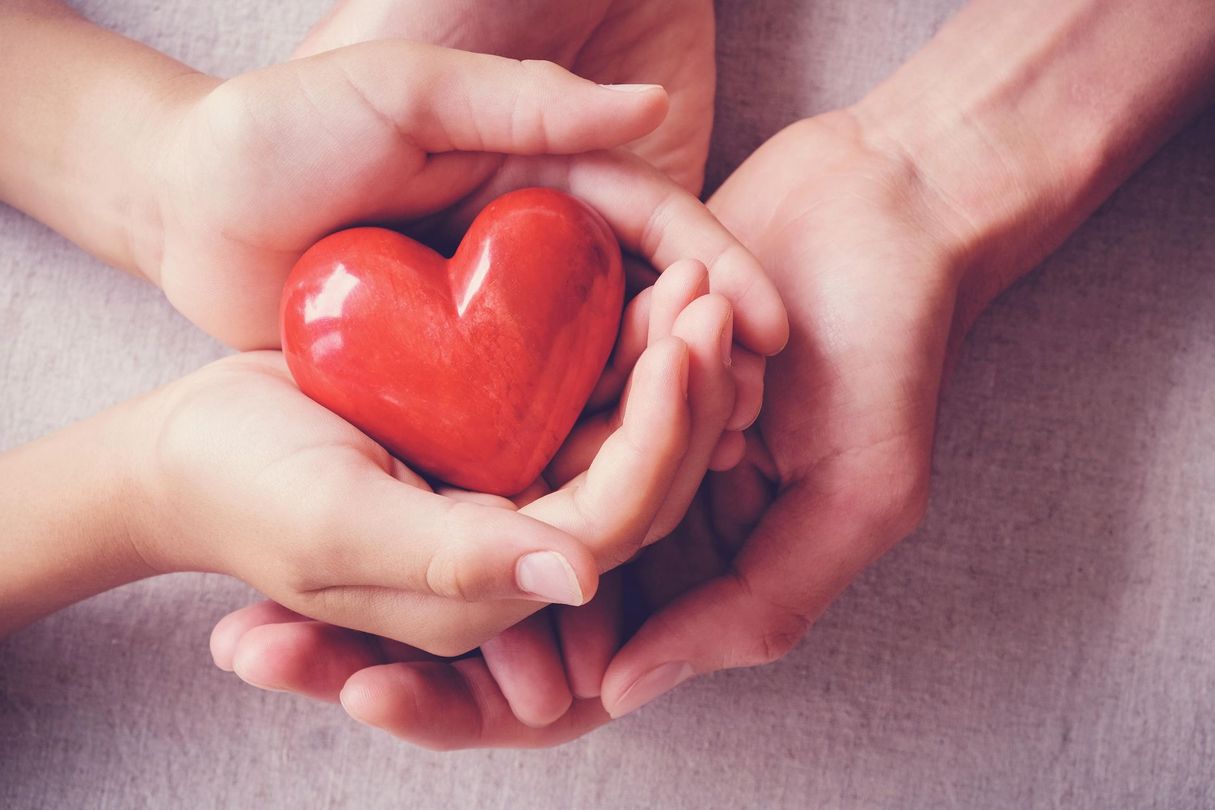 A woman and child are holding a red heart in their hands.