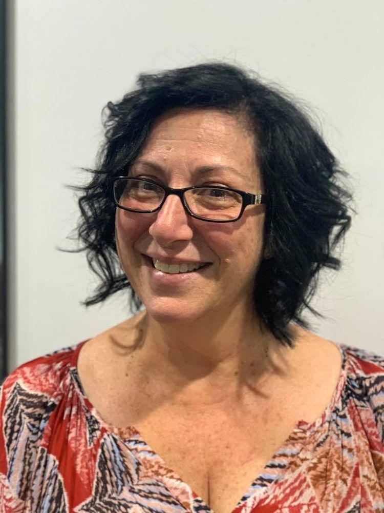 A Woman Wearing Glasses And A Red Shirt Is Smiling For The Camera — Sarina Hair Fashions in Sarina, QLD