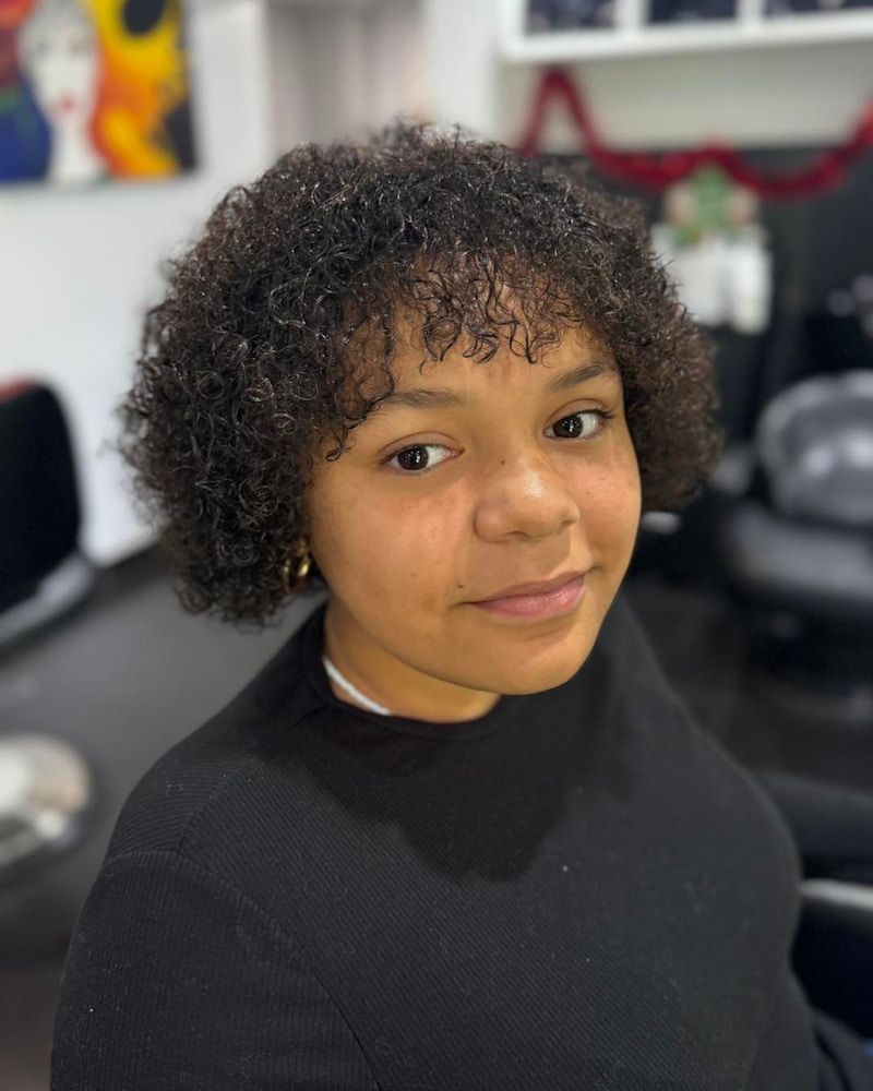 A Young Woman With Curly Hair Is Sitting In A Chair In A Room — Sarina Hair Fashions in Sarina, QLD