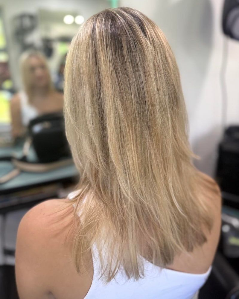 A Woman With Long Blonde Hair Is Sitting In Front Of A Mirror In A Salon — Sarina Hair Fashions in Sarina, QLD