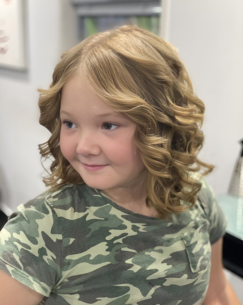 A Little Girl With Curly Hair Is Wearing A Camouflage Shirt — Sarina Hair Fashions in Sarina, QLD