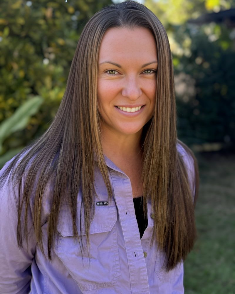 A Woman With Long Hair Is Wearing A Purple Shirt And Smiling — Sarina Hair Fashions in Sarina, QLD