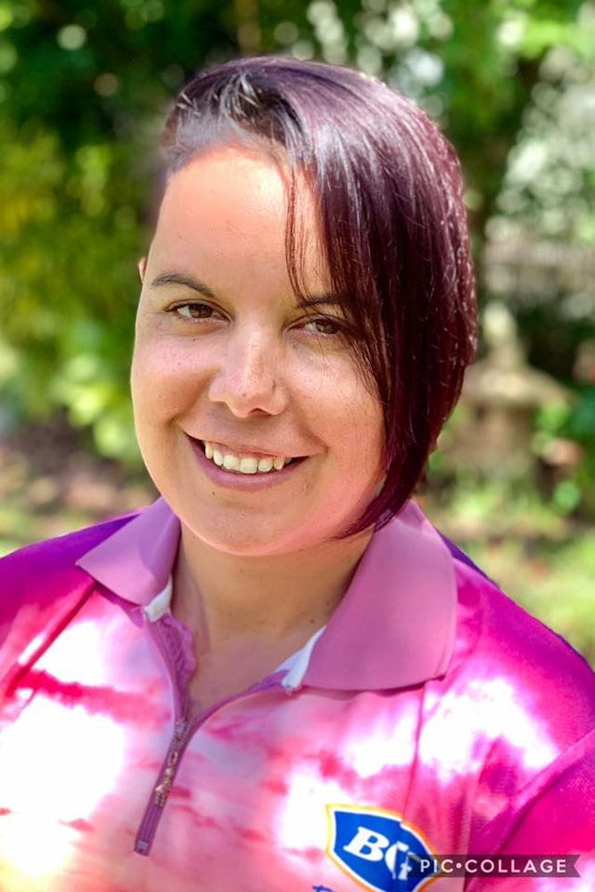 A Woman With Purple Hair Is Wearing A Pink Shirt And Smiling — Sarina Hair Fashions in Sarina, QLD