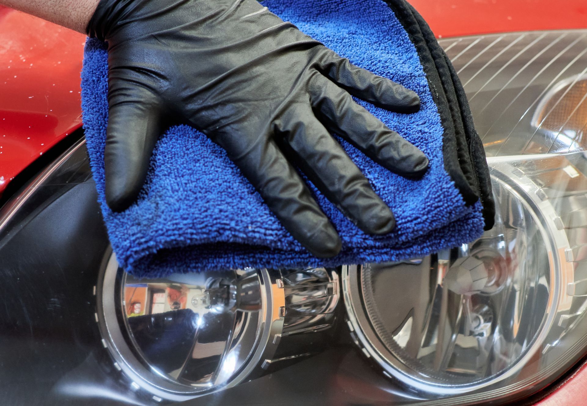 Gloved hand holding a blue microfiber cloth over a car's headlight, cleaning.