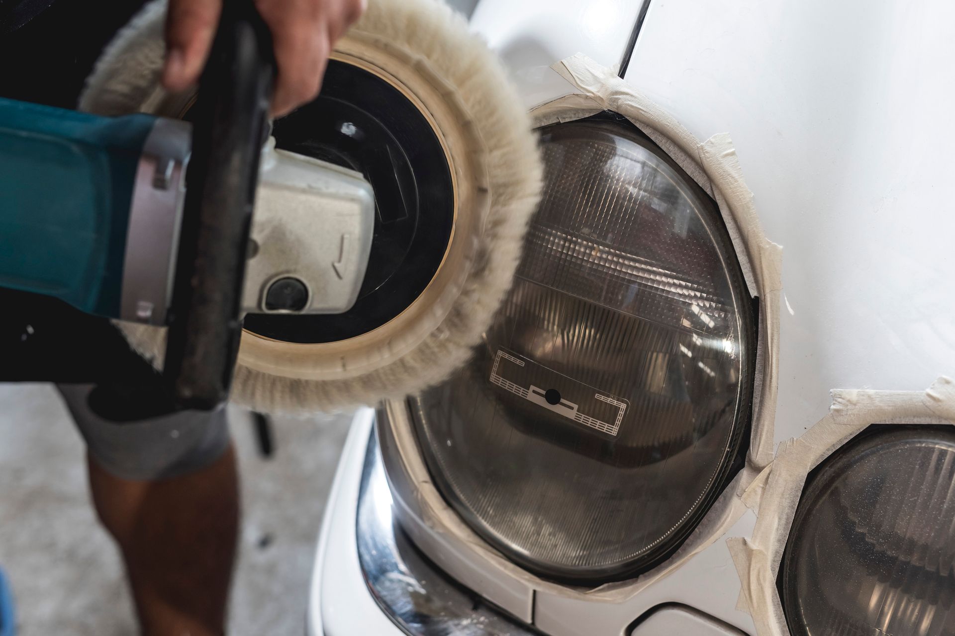 Person polishing a car headlight with a power buffer.