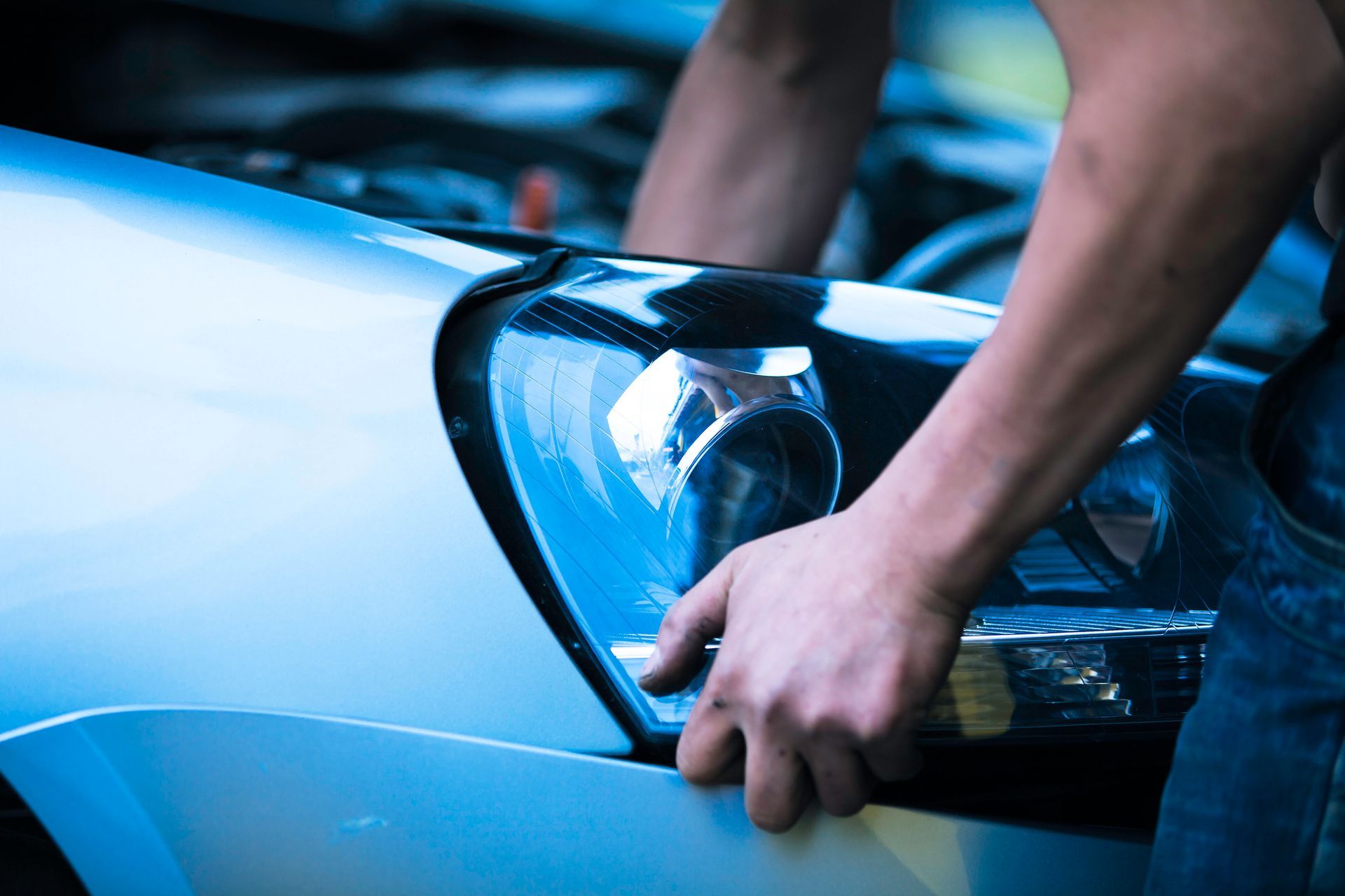 A person's hands are installing a car headlight on a car's front, the hood is open.
