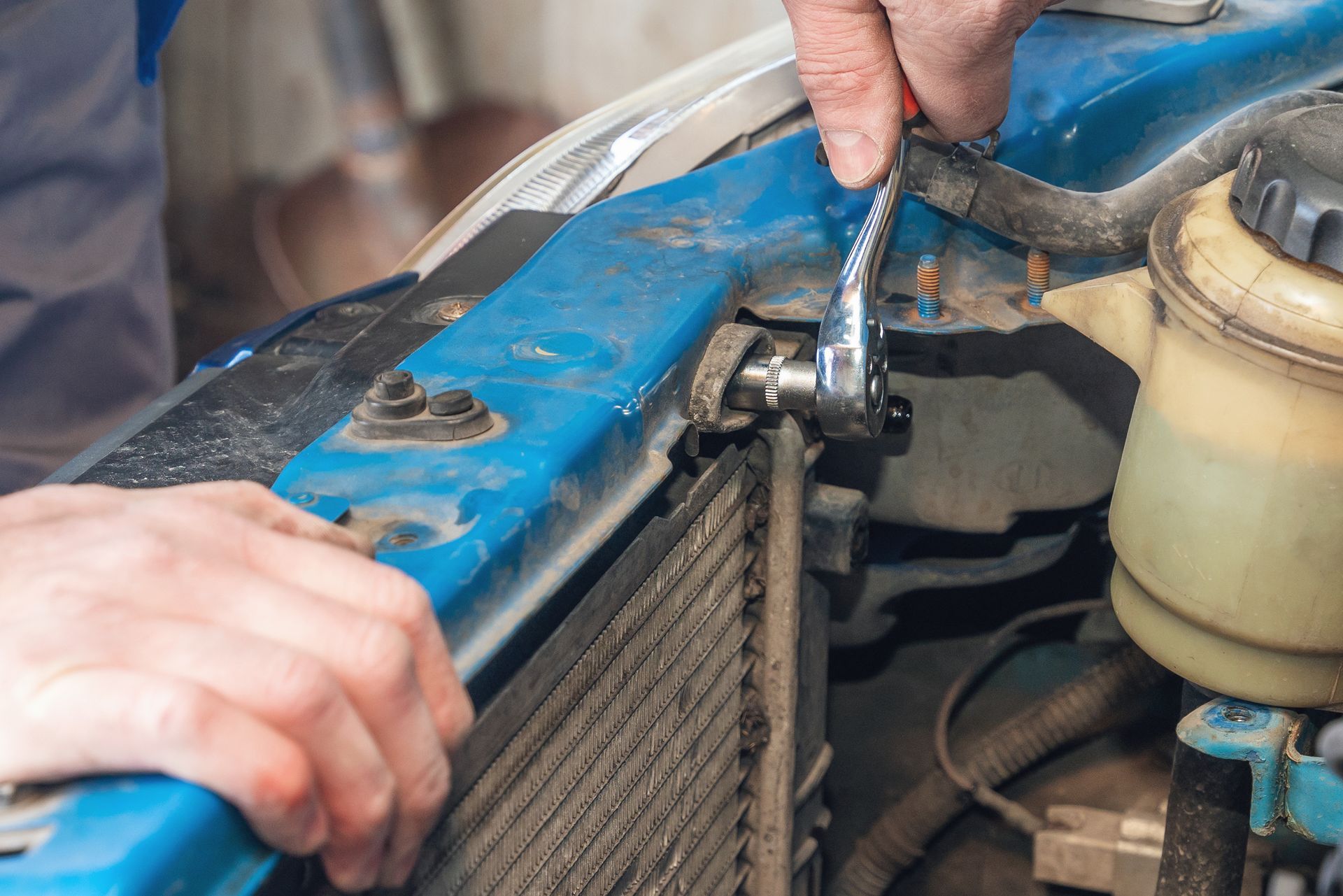 Hands using a wrench to tighten a bolt on a blue car part near the radiator.
