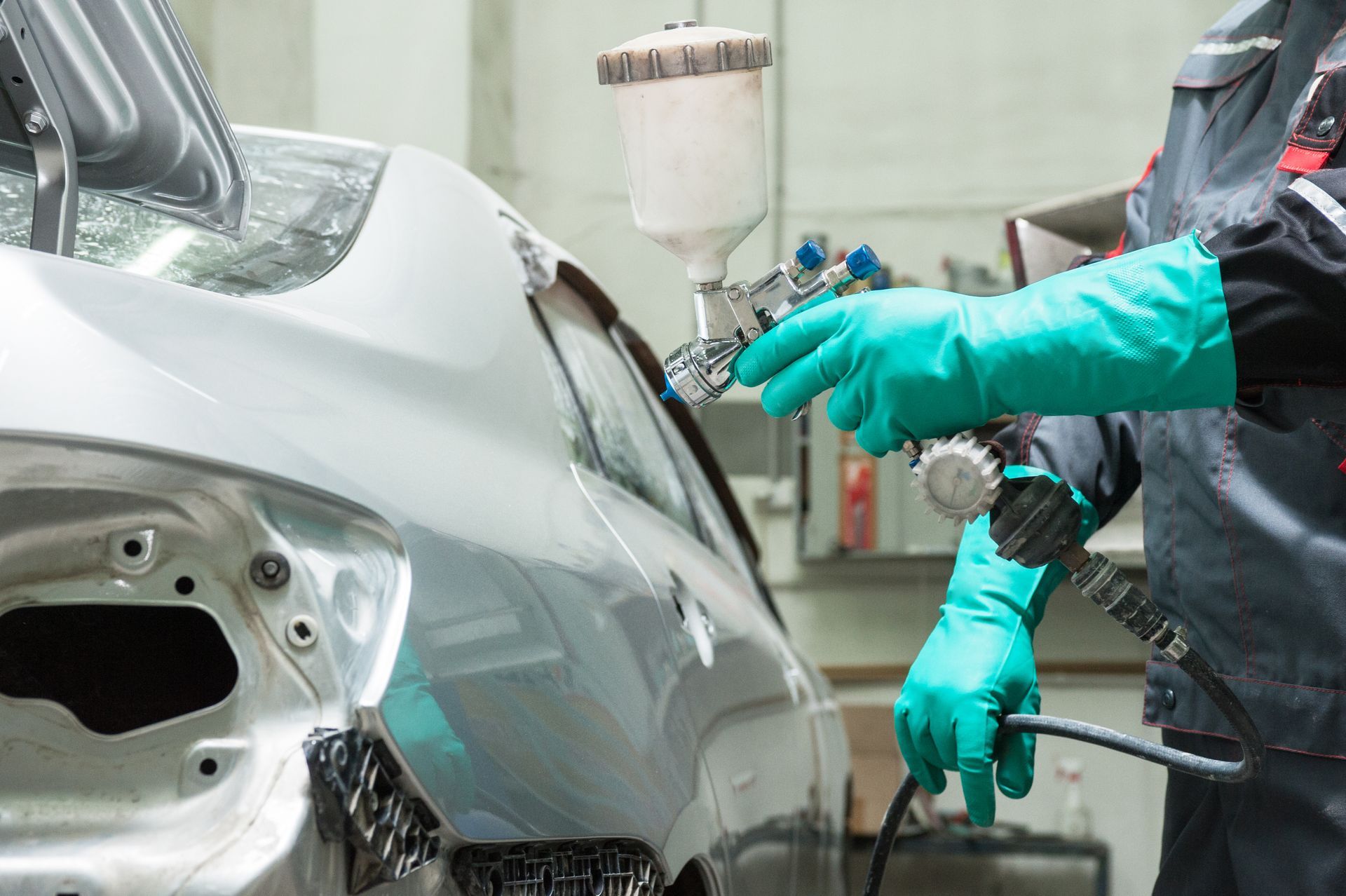 Person in gloves spray painting a car in a garage.