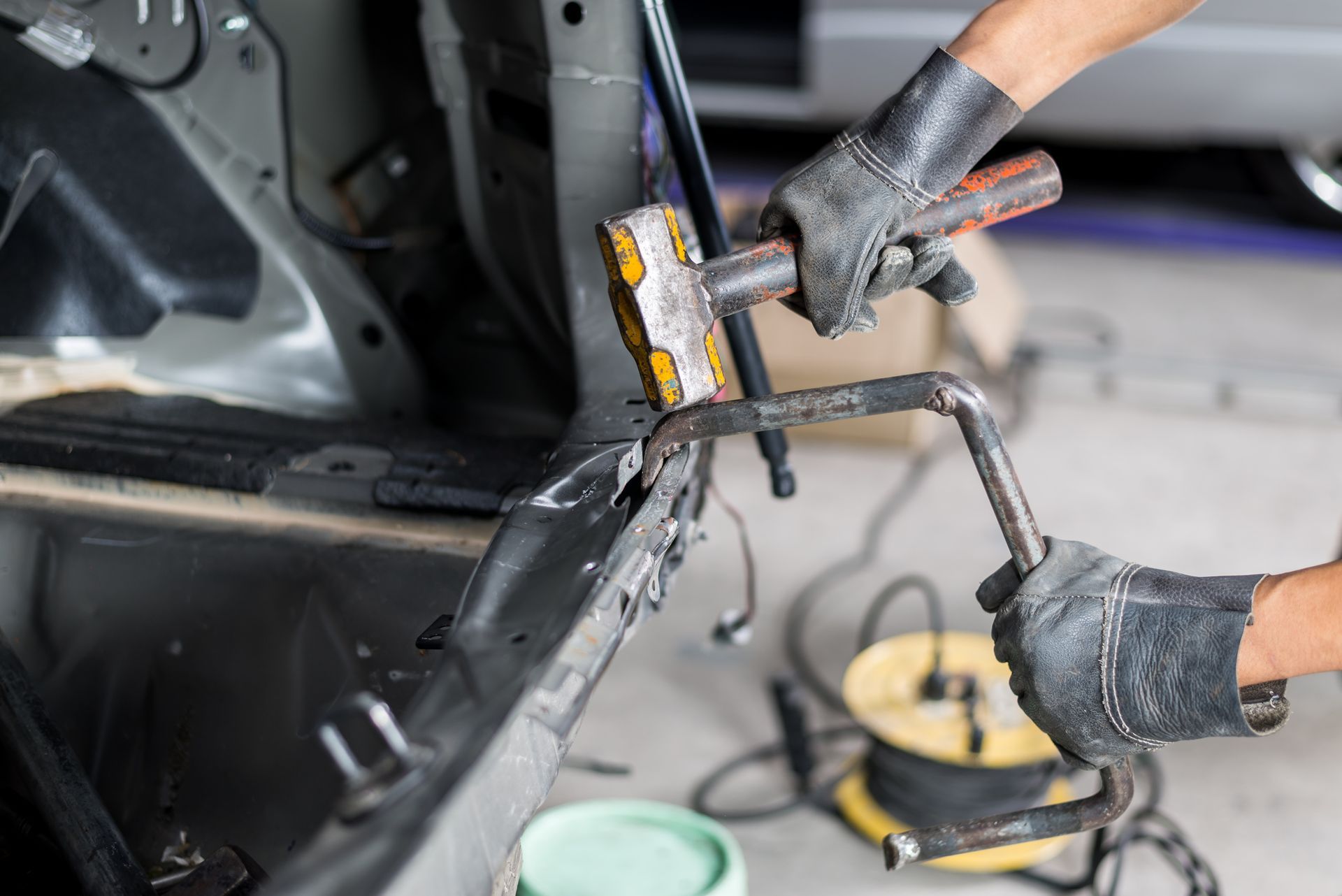Person in gloves hammering car frame with a tool.