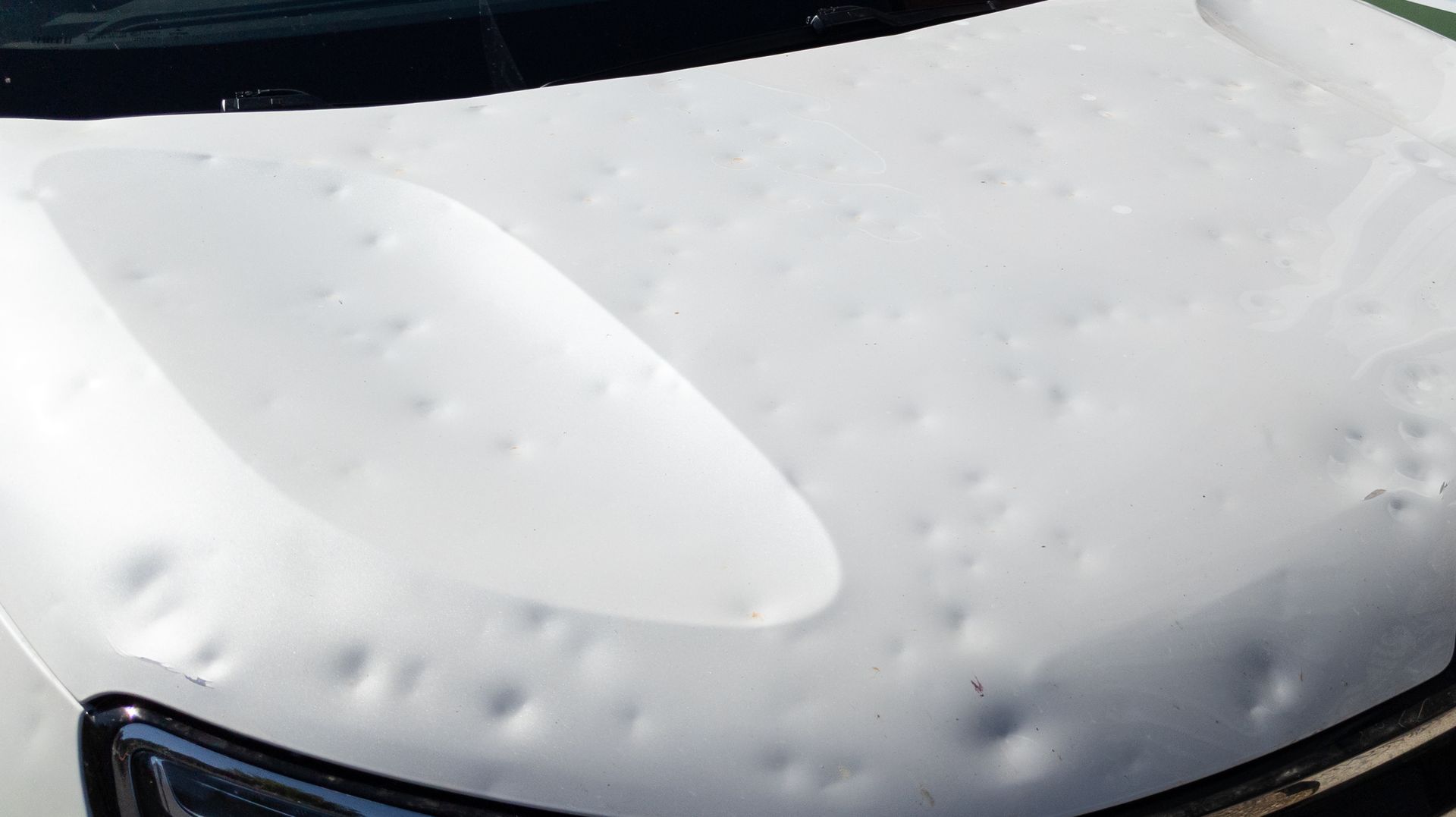 White car hood, severely dented from hail damage.