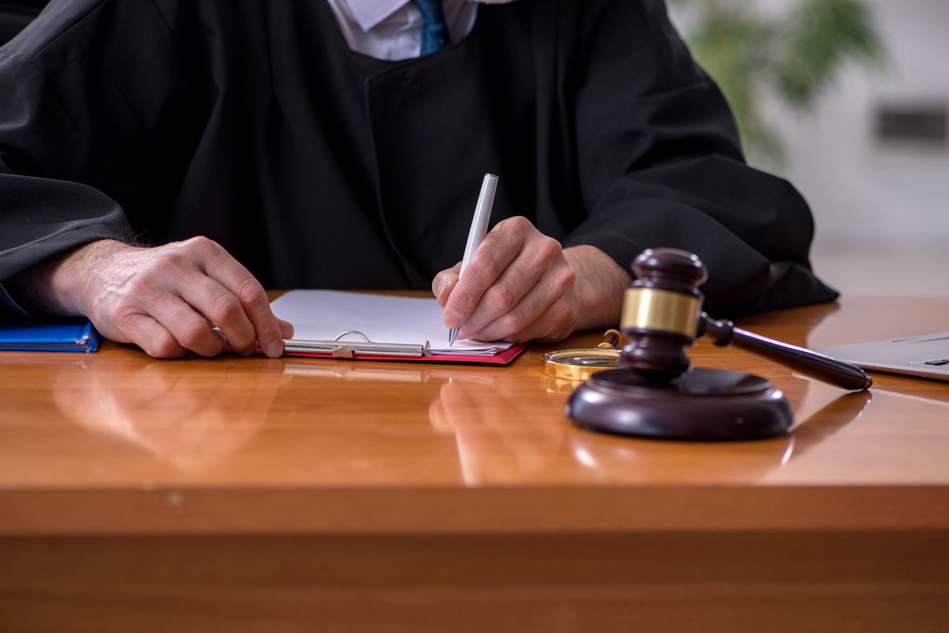 Judge writing on documents at a wooden desk with a gavel in the foreground