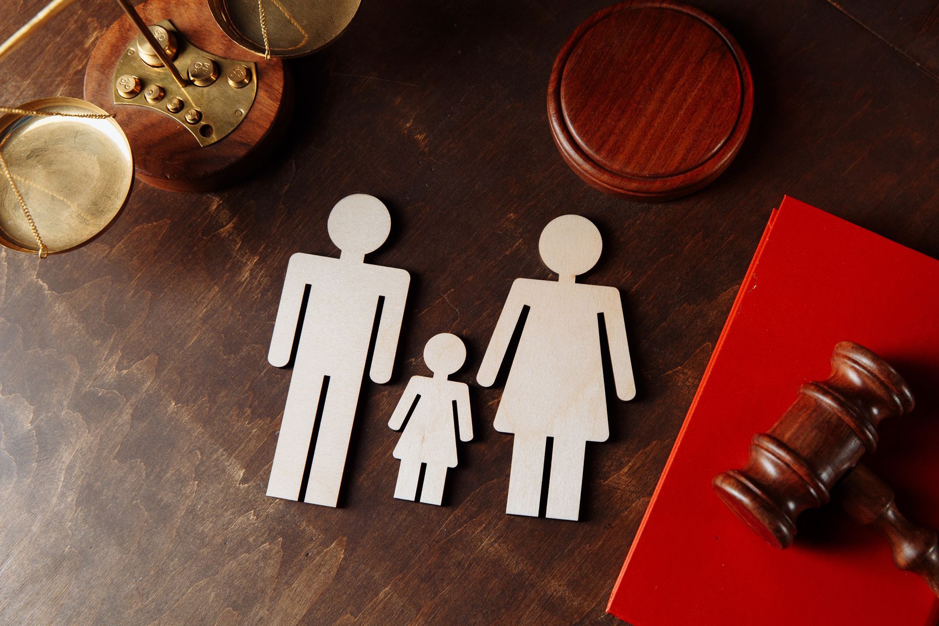 Wooden family figures with scales, gavel, and red book on a brown surface.