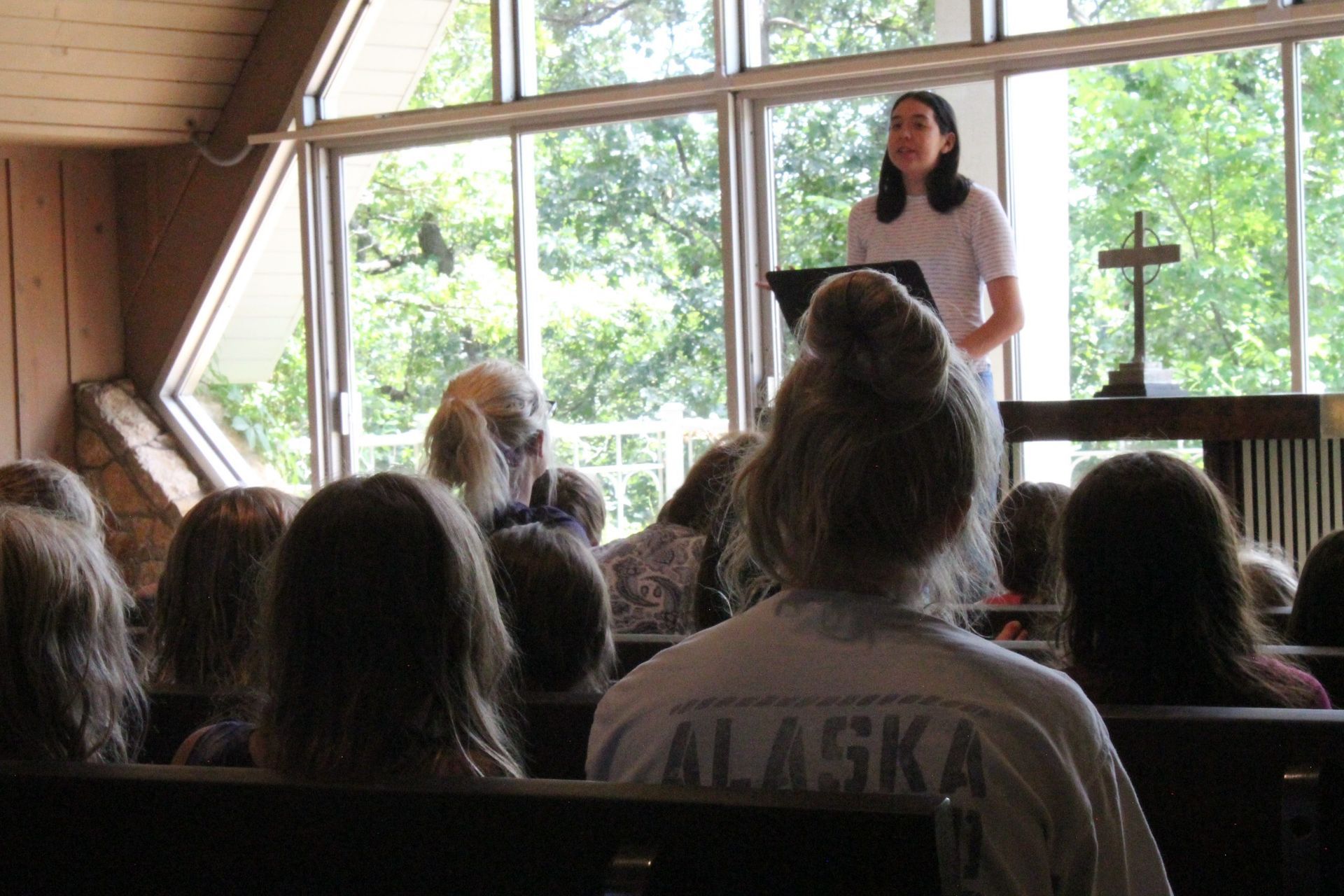 A woman is giving a speech in front of a group of people wearing alaska shirts