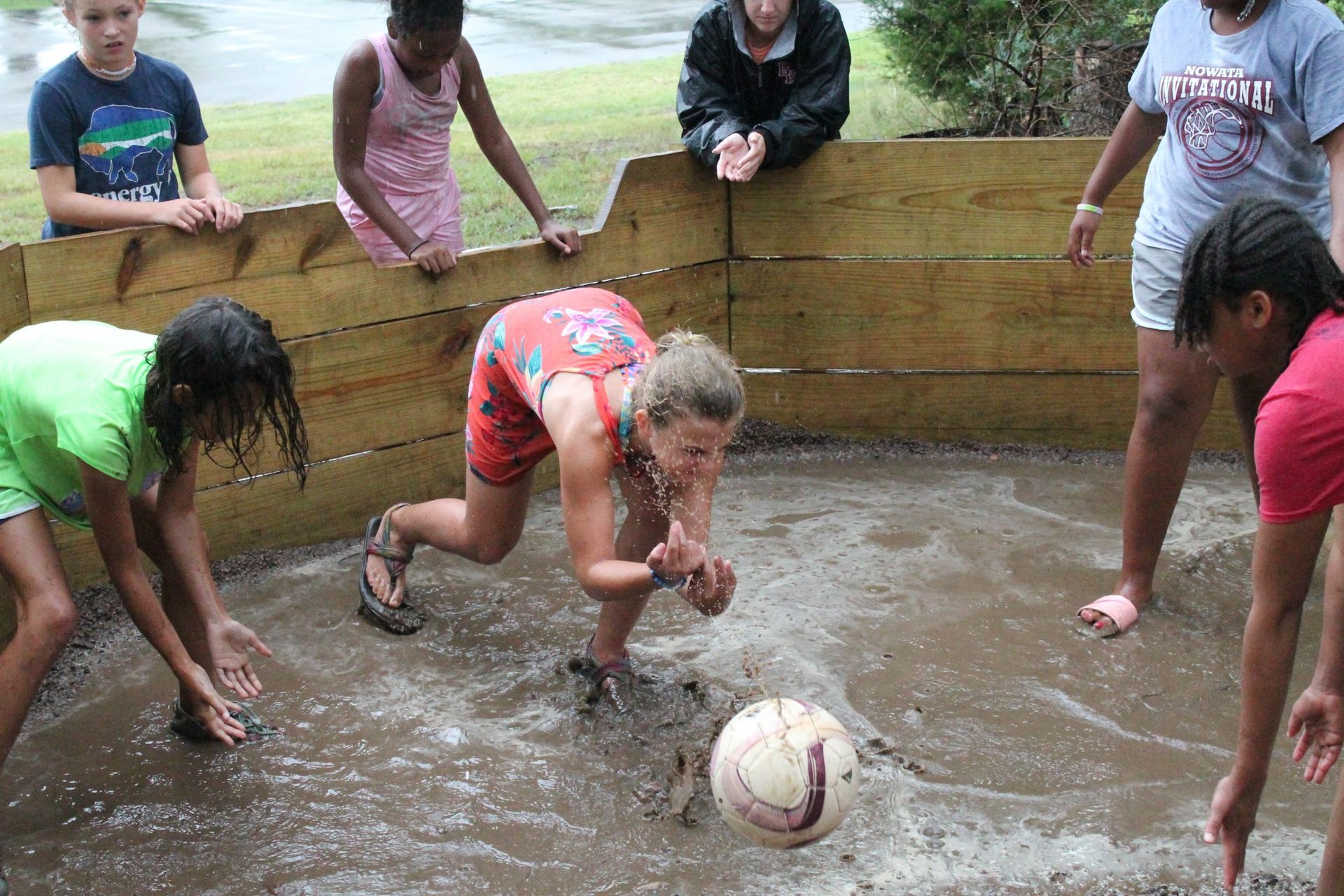 A group of children are playing soccer in the mud.