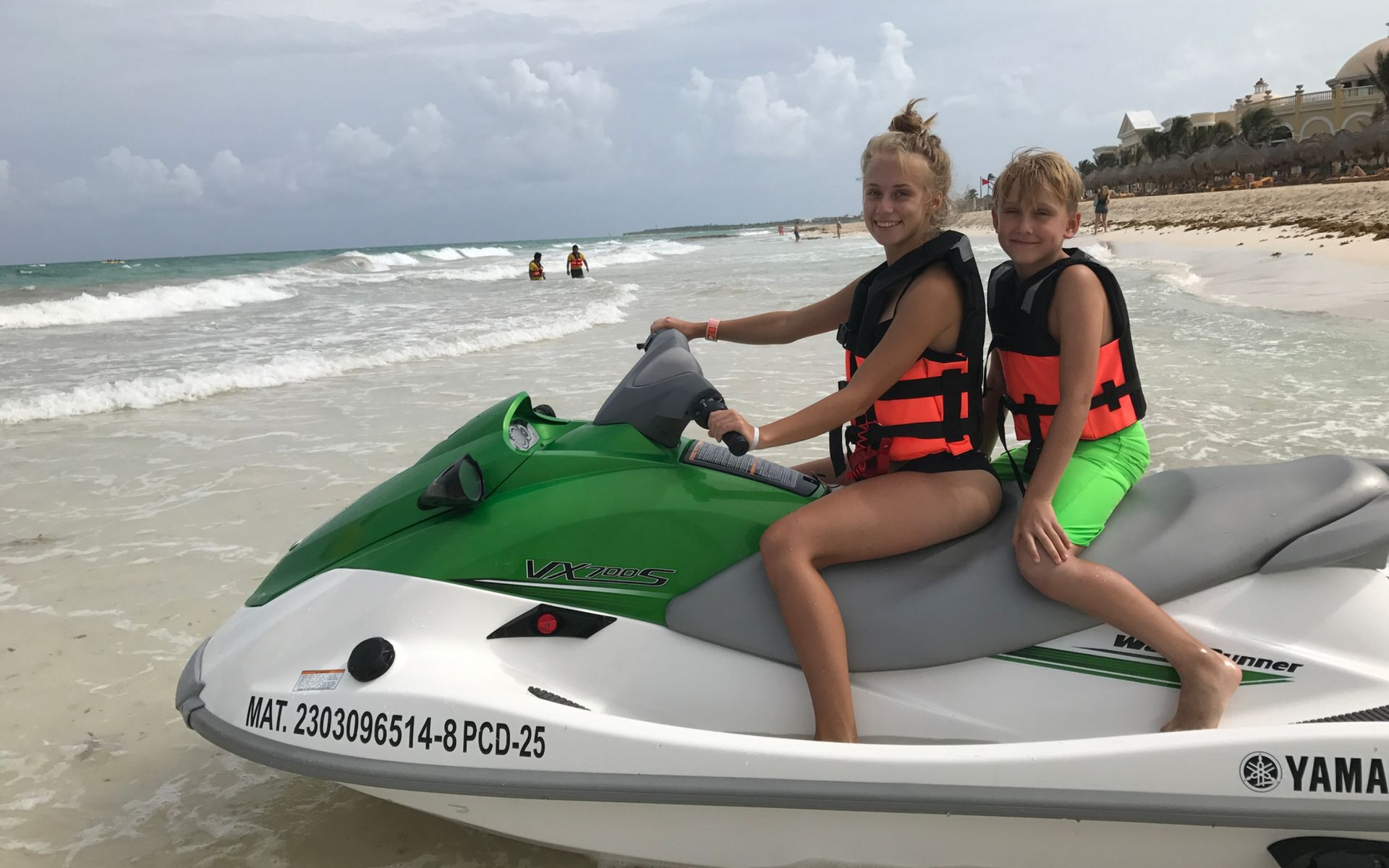 a girl and a boy sitting on a jet ski on a beach