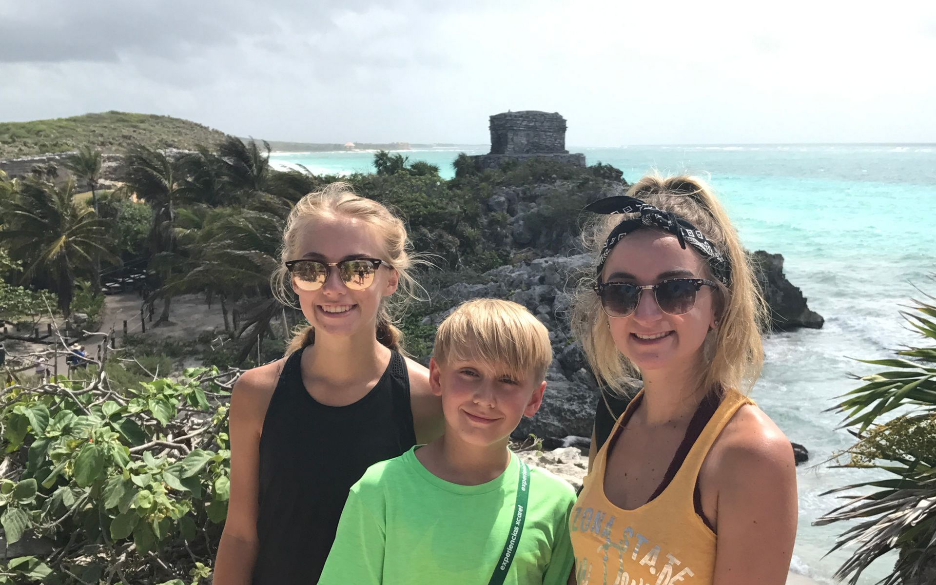 2 girls and one boy standing on a cliff over turquoise ocean and ancient ruins